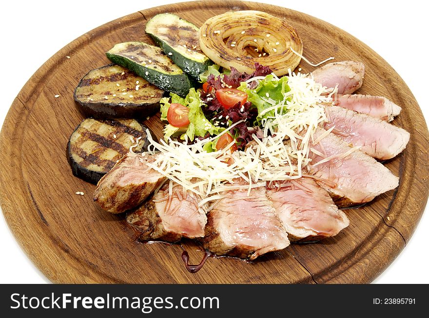 Meat roasted on a grill with vegetables on a wooden plate