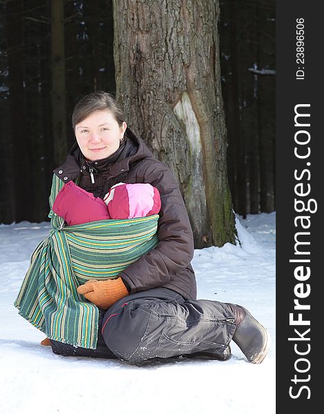 Sitting mother with newborn baby in the sling in winter