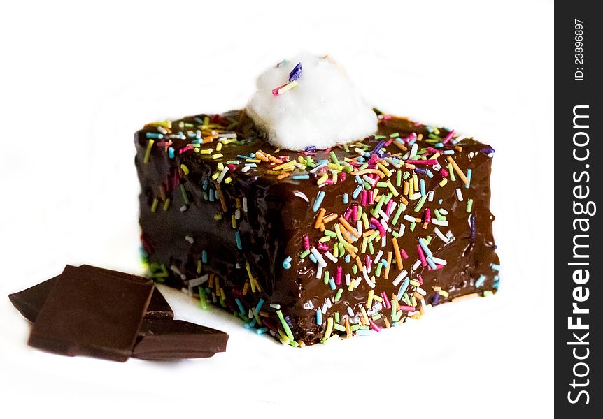 Chocolate cake with cream on top, multicolored sugar topping on sides and pieces of chocolate on the left on white background