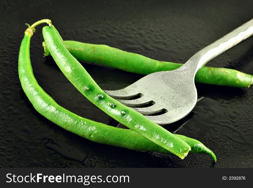 Fresh green beans pierced with a fork on a watery black plate