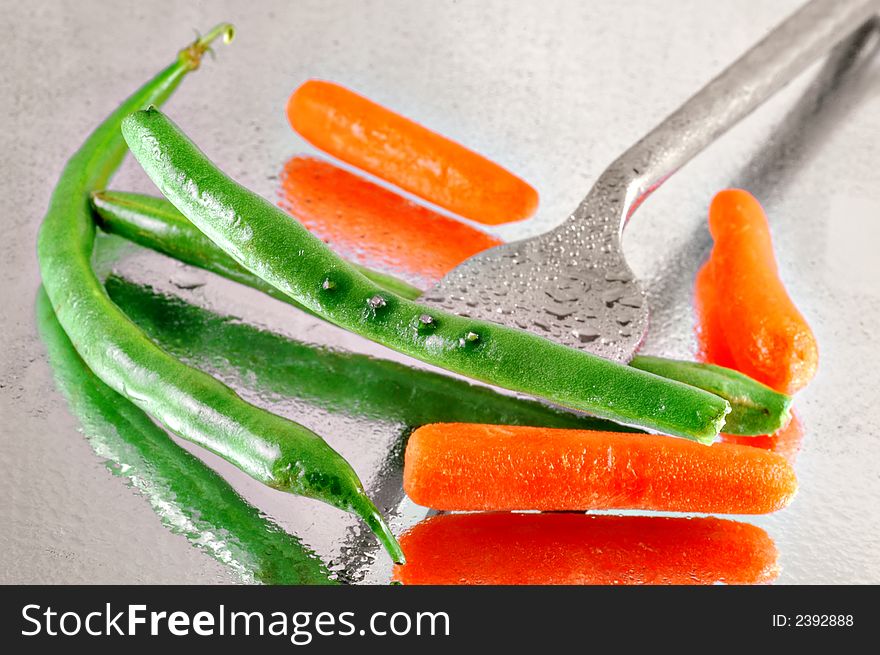 Fresh green beans and baby carrots pierced with a fork on a reflective watery mirrored background. Fresh green beans and baby carrots pierced with a fork on a reflective watery mirrored background