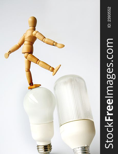 Wooden mannequin walking on two different lightbulbs. Wooden mannequin walking on two different lightbulbs