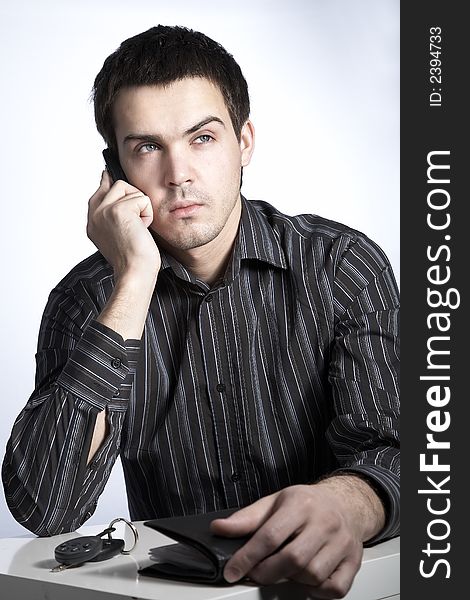 Serious young man with car keys and wallet speaking phone. Serious young man with car keys and wallet speaking phone