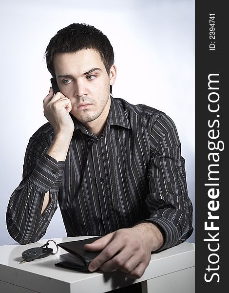 Serious young man with car keys and wallet speaking phone. Serious young man with car keys and wallet speaking phone