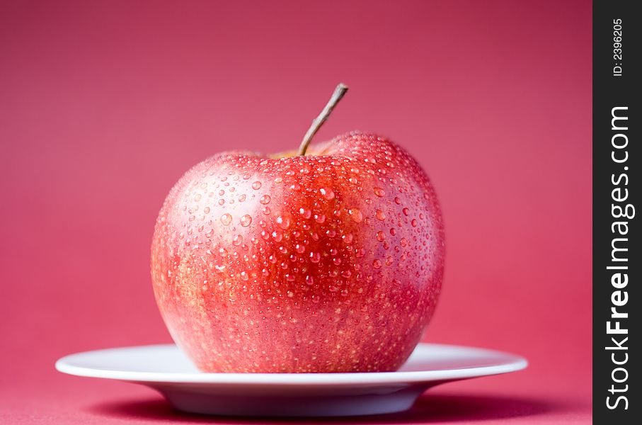 Red apple with drops of water, red background