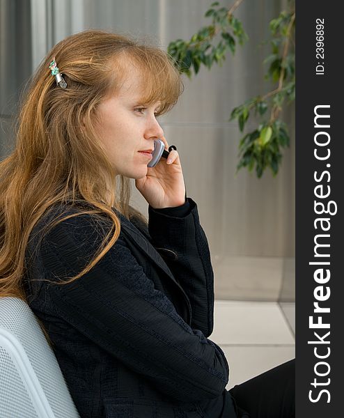 The girl speaks by phone, sitting in an armchair in a hall of office building