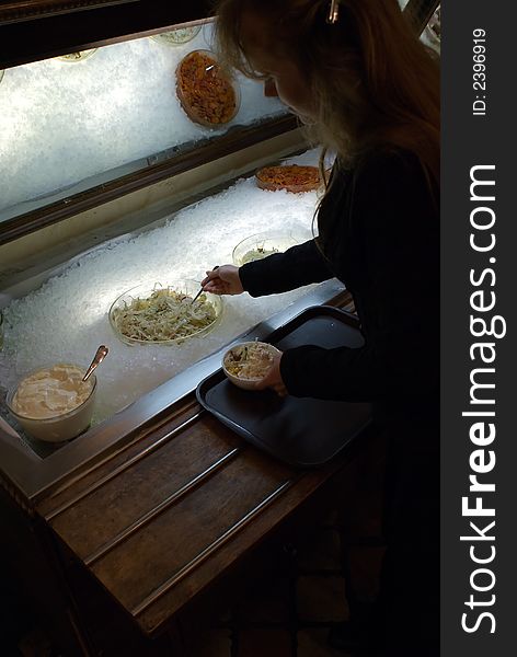 The girl lays down salad in a plate from the big bowl. The girl lays down salad in a plate from the big bowl