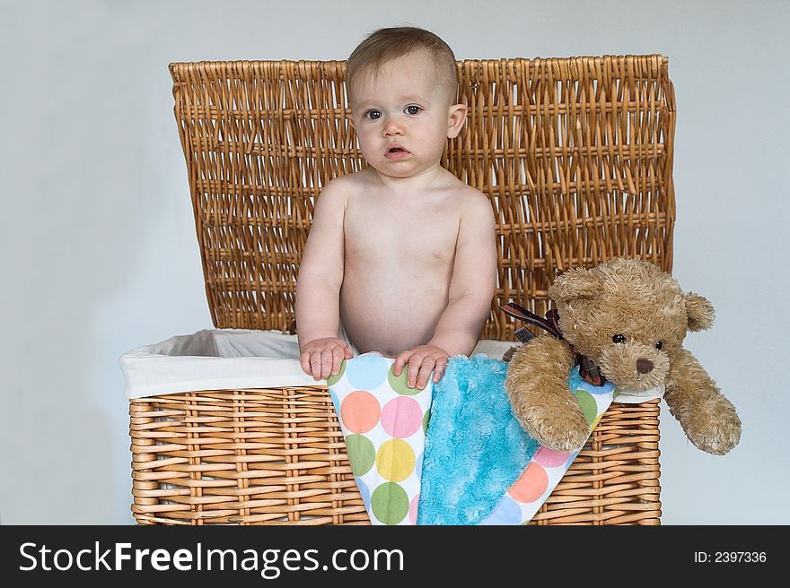 Image of cute baby and teddy bear peeking out of a wicker trunk