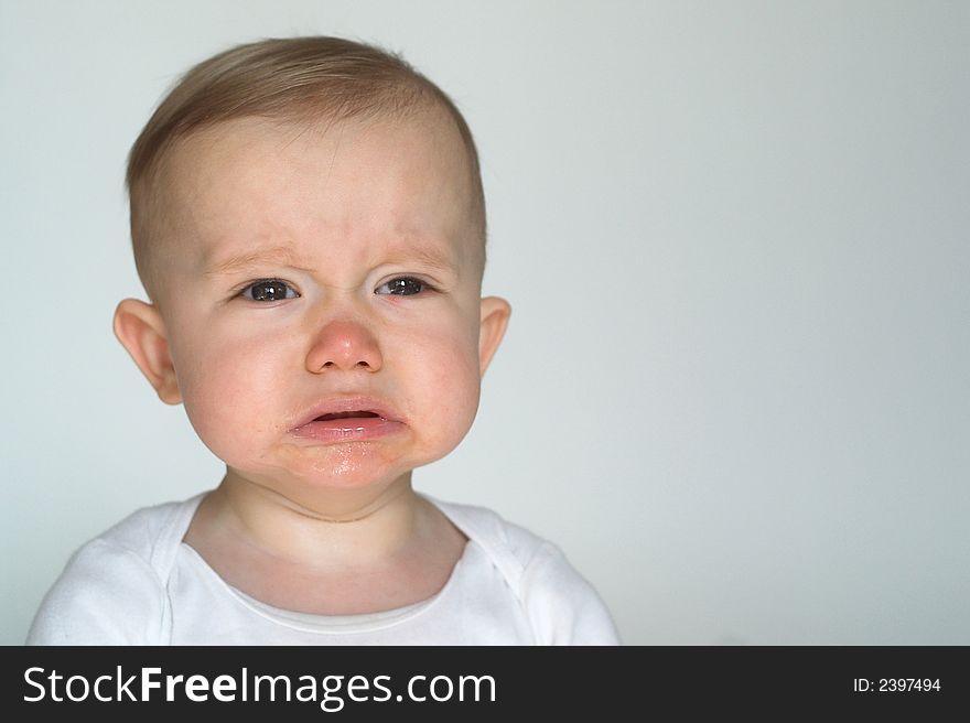 Image of cute whining baby sitting in front of a white background. Image of cute whining baby sitting in front of a white background