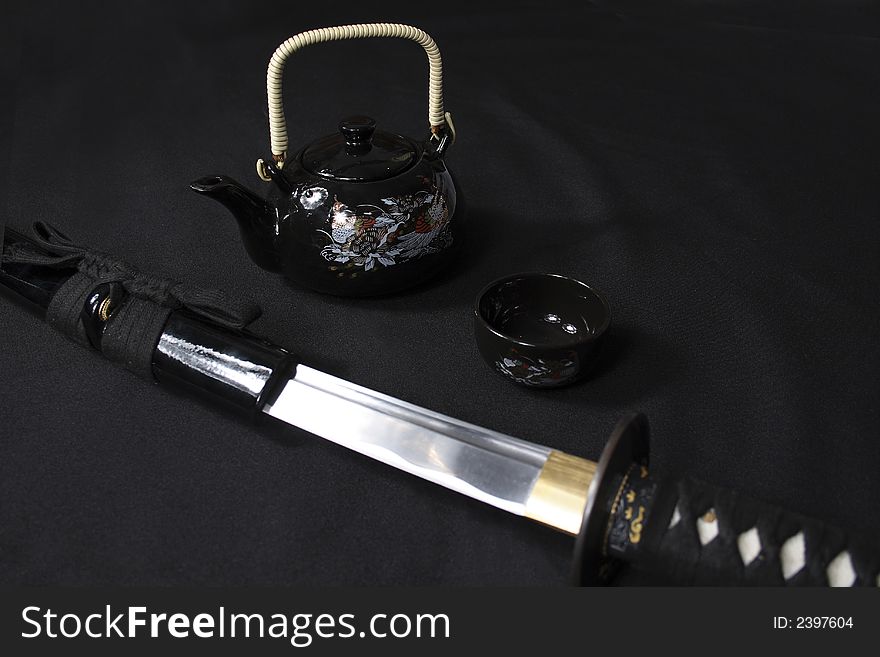 Japanese sword in sheath with cup and teapot on the black background. Japanese sword in sheath with cup and teapot on the black background