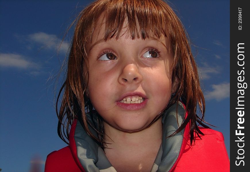 Color photo close up of little girl against blue sky, wearing lifejacket. Still a little wet from being in lake. Color photo close up of little girl against blue sky, wearing lifejacket. Still a little wet from being in lake.