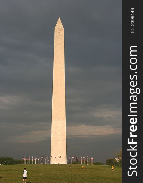 The sun is reflecting off of the Washington monument with a dark cloudy sky behind it.