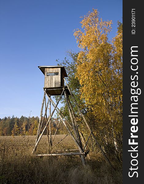 Wooden shelter for hunters, hunting shelter on the edge of the forest, with yellow birch leaves, autumn landscape with blue sky, brown plowed fields, forest land and fields. Wooden shelter for hunters, hunting shelter on the edge of the forest, with yellow birch leaves, autumn landscape with blue sky, brown plowed fields, forest land and fields