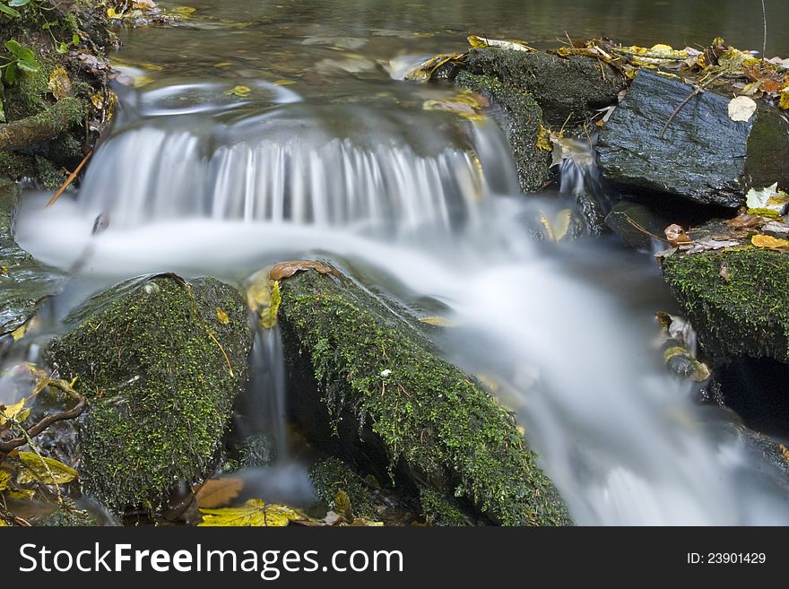 Waters of the Czech Republic, weir on the stream between the rocks, fallen colorful leaves on the stones, moss covered stones, close to the water fall weir