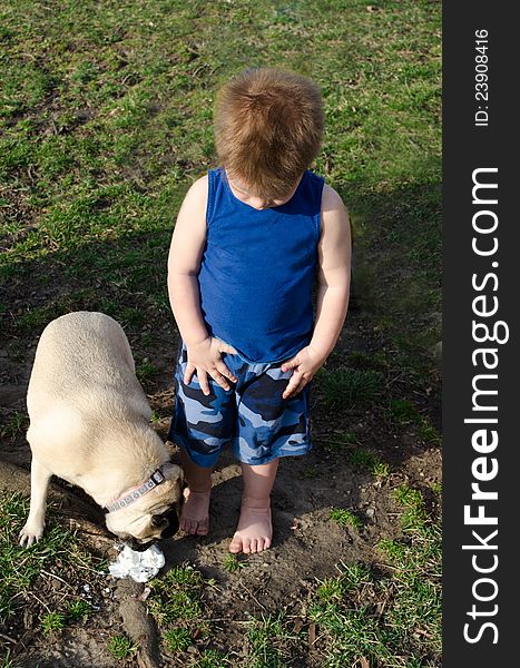 Little boy looks down at his feet at a mess of ice cream his dog is happily eating up. Little boy looks down at his feet at a mess of ice cream his dog is happily eating up
