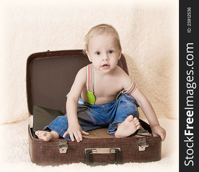 The child sits in jeans on a suitcase barefoot and smiles. The child sits in jeans on a suitcase barefoot and smiles