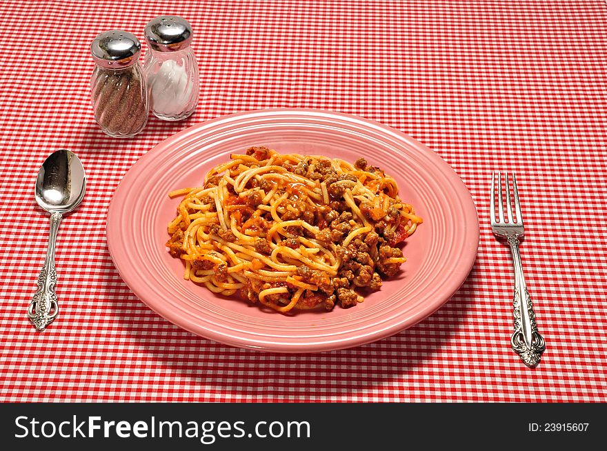 A plate full of spaghetti on a red check table cloth