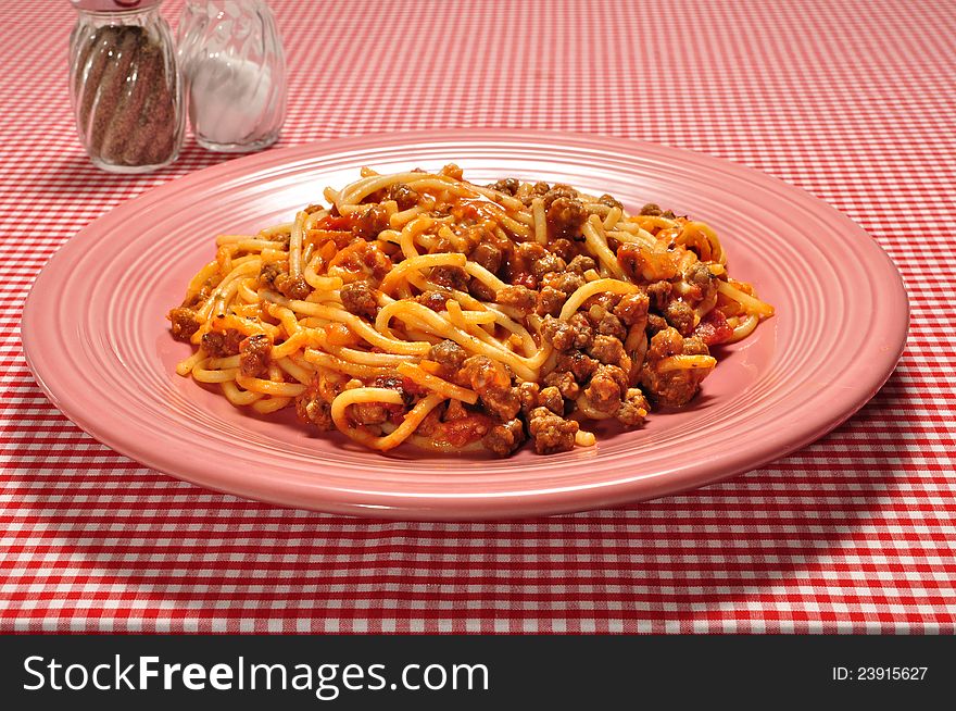 A plate full of spaghetti on a red check table cloth