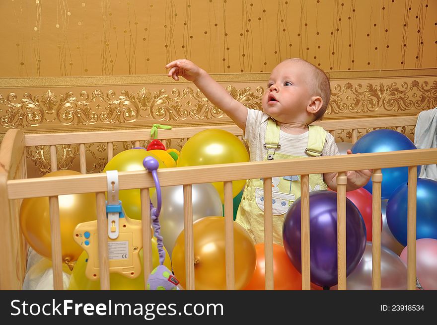 The child in a bed with balloons of different color against wall-paper