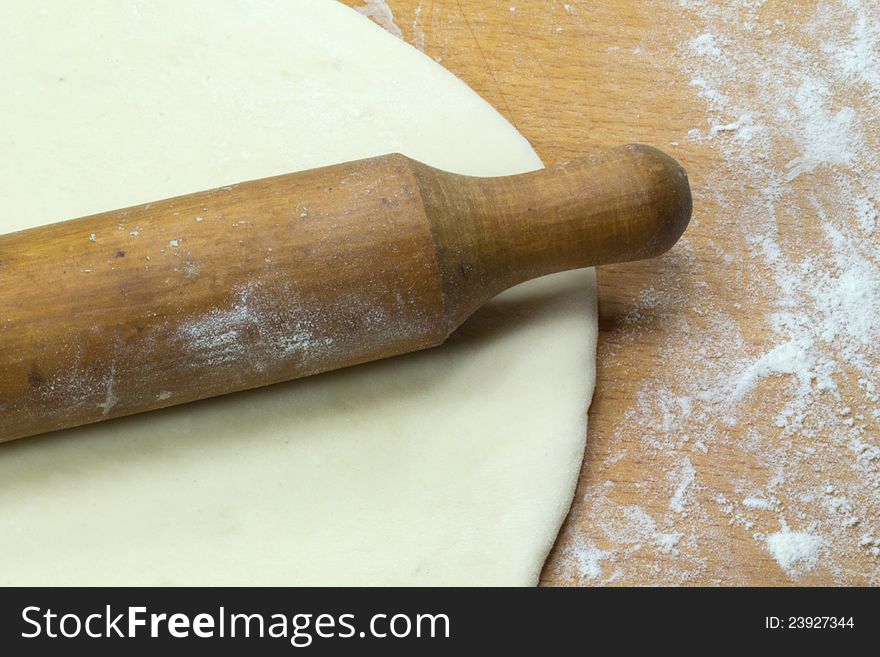 Rolled out dough and rolling pin lying on a wooden board sprinkled with flour