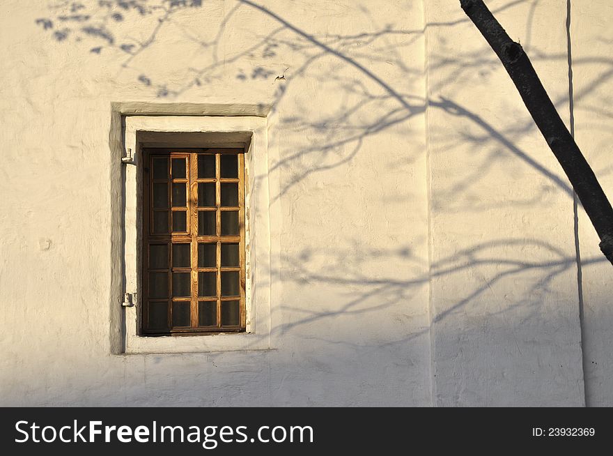 Wooden window with evening tree shadow over whitewashed wall