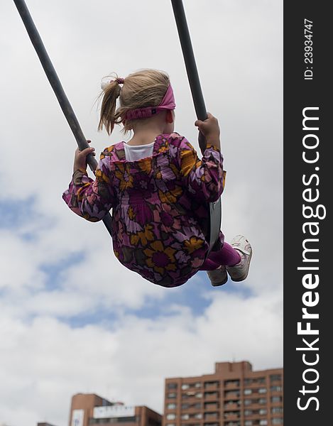 Little girl swinging with buildings in the background. Little girl swinging with buildings in the background