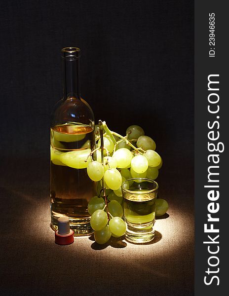 Bunch of grapes near bottle of white wine and wineglass on dark background. Bunch of grapes near bottle of white wine and wineglass on dark background