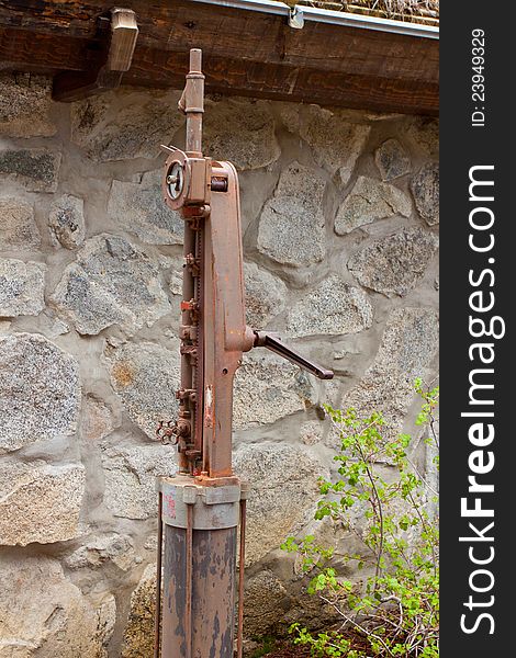 A pump for an old well is rusted and weathered outside a vintage home. A pump for an old well is rusted and weathered outside a vintage home.