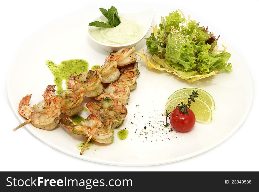 Skewers of shrimp on a white plate with vegetables and lemon