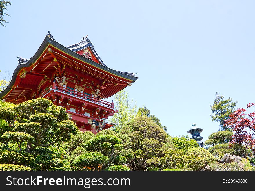 A bright red Japanese pagoda building in a tea garden sits peacefully.