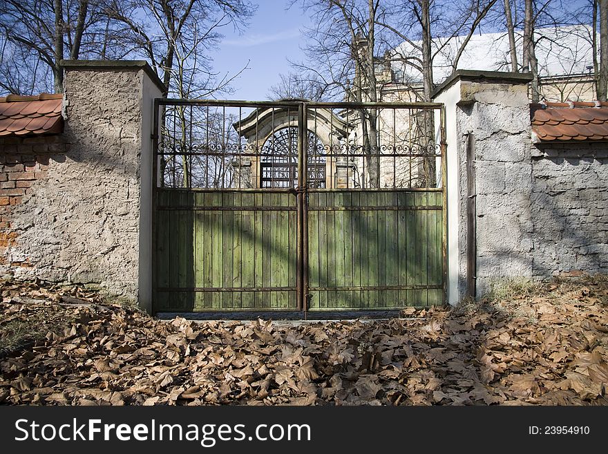 Green gateway to the park, gateway between a stone wall, gateway between a stone wall, dry brown leaves on the ground in front of the gate, detail of the castle gates in a sunny day, autumn day in the park