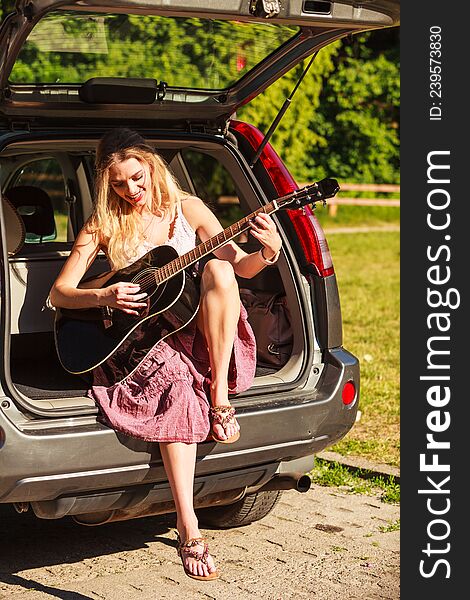 Travel vacation hitchhiking concept. Summer girl hippie style sitting on hatchback car with acoustic guitar. Travel vacation hitchhiking concept. Summer girl hippie style sitting on hatchback car with acoustic guitar