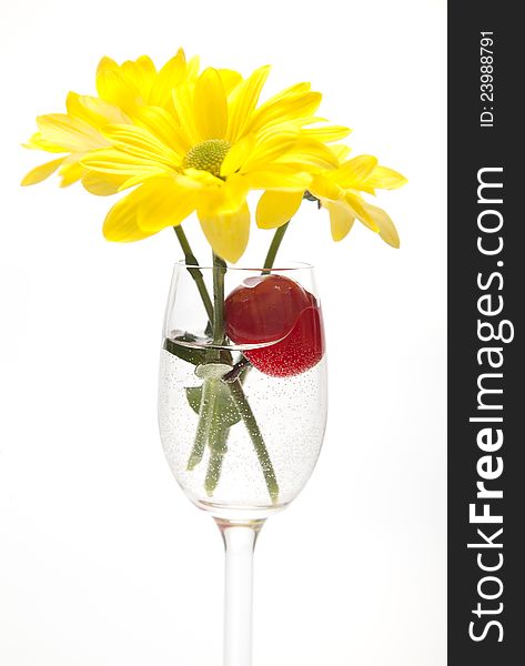 A glass, cherry and yellow flowers on a white back