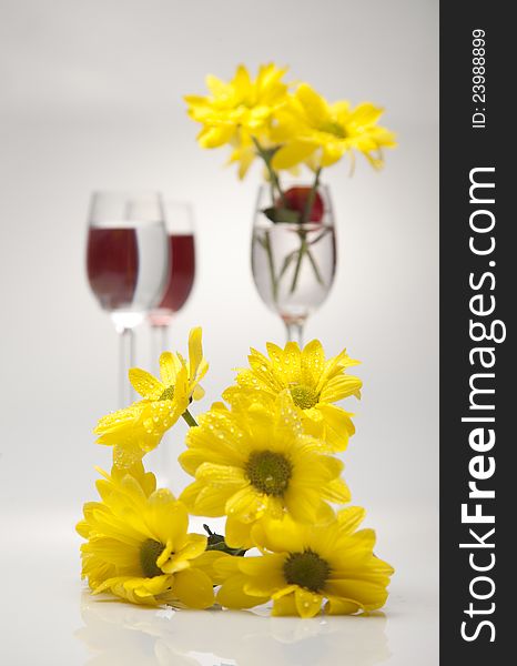 A glass, cherry and yellow flowers on a white back