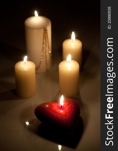 Candles on a dark background. One candle is in the form of the heart.