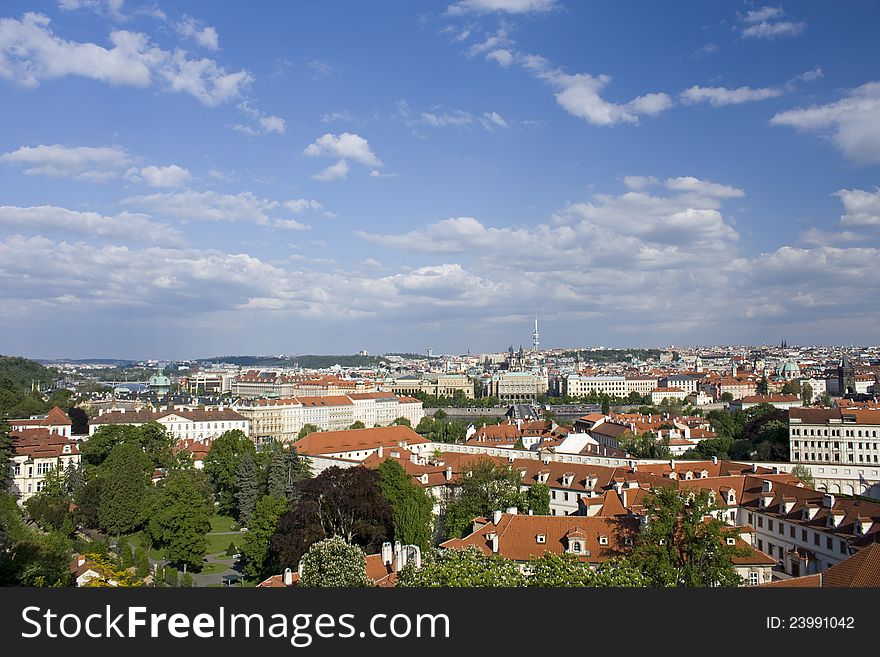 View on the roofs of thresholds , blue sky with clouds above prague , sunny summer day in prague , green vegetation between houses , the red roofs of the houses in prague. View on the roofs of thresholds , blue sky with clouds above prague , sunny summer day in prague , green vegetation between houses , the red roofs of the houses in prague