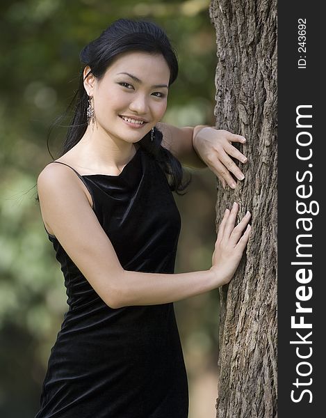 A beautiful young chinese woman poses next to a tree in a black evening gown. A beautiful young chinese woman poses next to a tree in a black evening gown