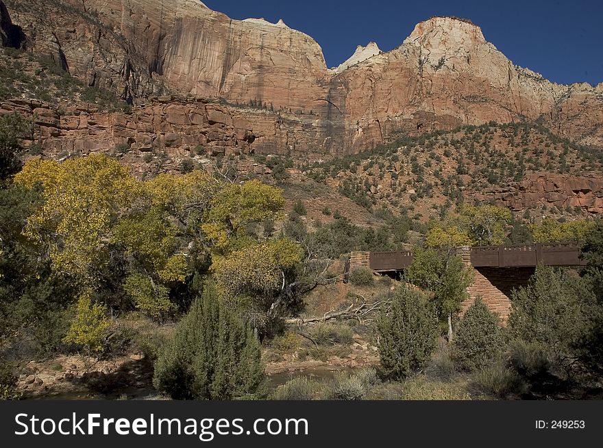 A full view of a canyon at Zion National Park. A stream is running in the foreground with towering rock cliffs above. A full view of a canyon at Zion National Park. A stream is running in the foreground with towering rock cliffs above.