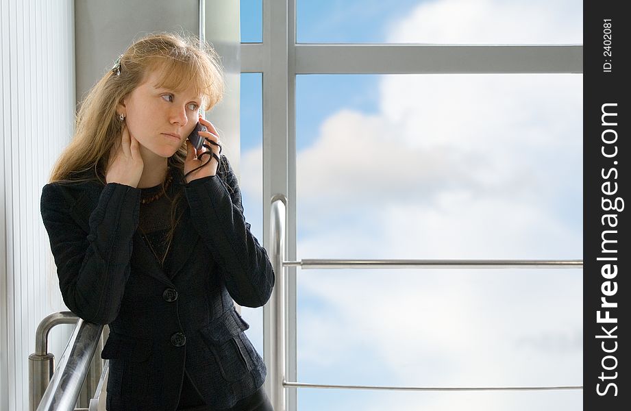 The girl speaks by phone, costing in office building near a window