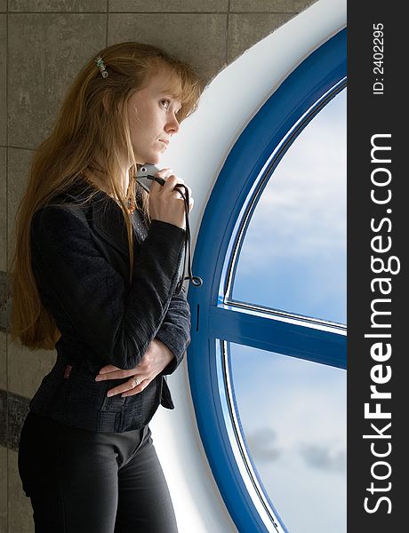 The girl with phone costs near a window in office building. The girl with phone costs near a window in office building