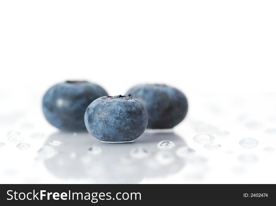 Three blueberries on a white surface with water drops. Three blueberries on a white surface with water drops.