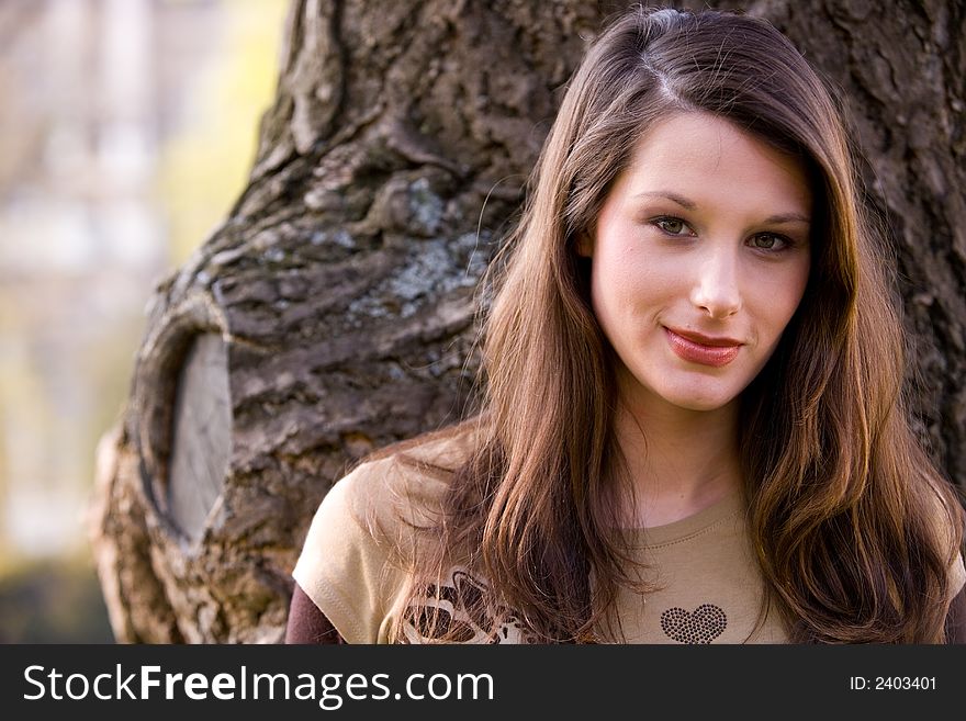 Beautiful young woman is standing in front of a tree. Beautiful young woman is standing in front of a tree