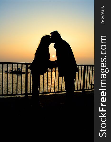 Silhouette couple kissing at sunset by the coast. Silhouette couple kissing at sunset by the coast