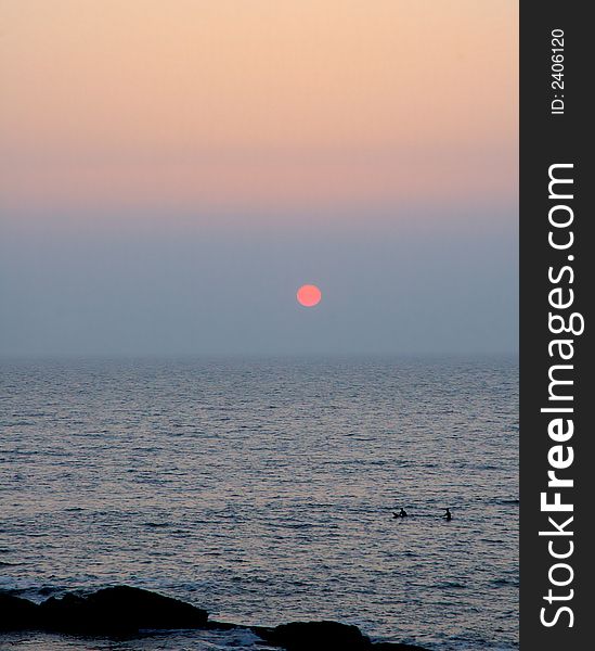 Surfers watching the pink sun going down. Surfers watching the pink sun going down