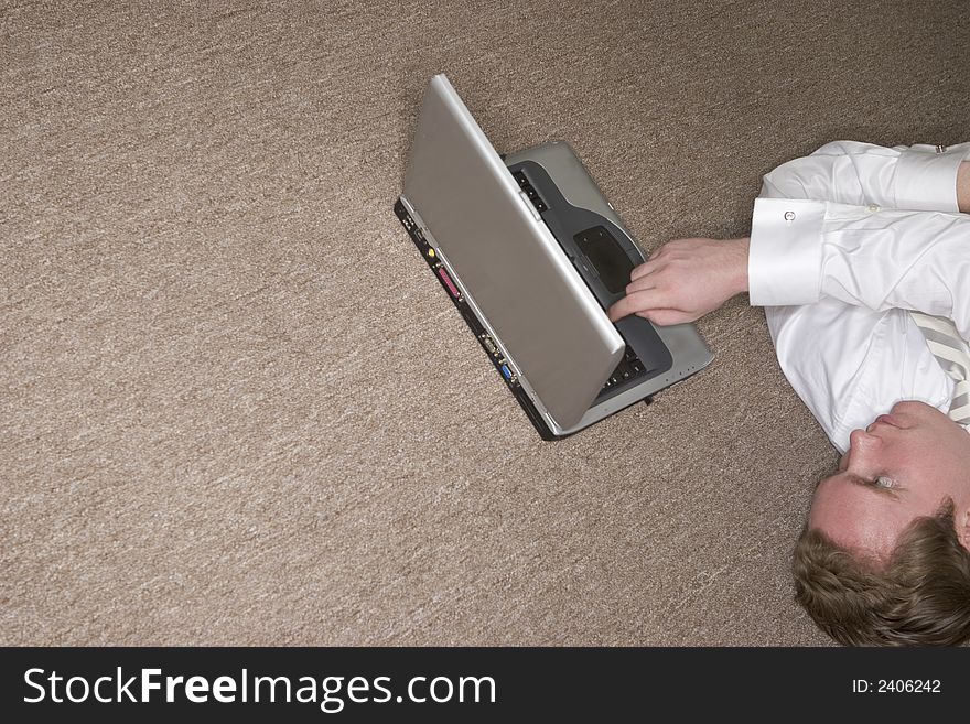 Businessman tired and stressed uses his laptop with one finger while lying on the floor. Businessman tired and stressed uses his laptop with one finger while lying on the floor