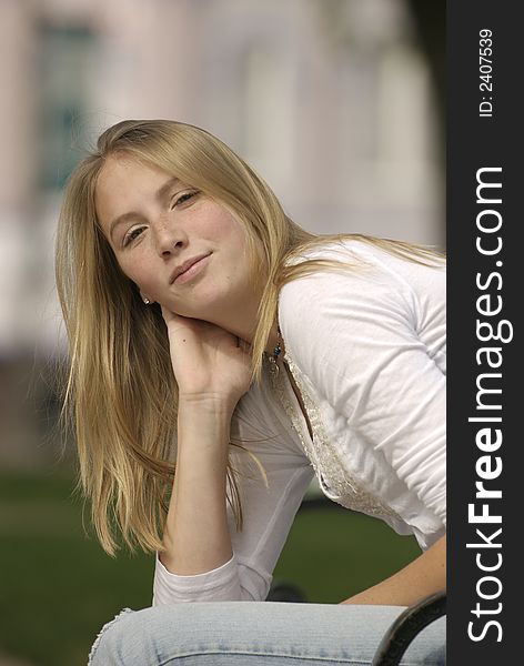 A caucasian female American teenager sits on a park bench on the Square in a small Texas town.