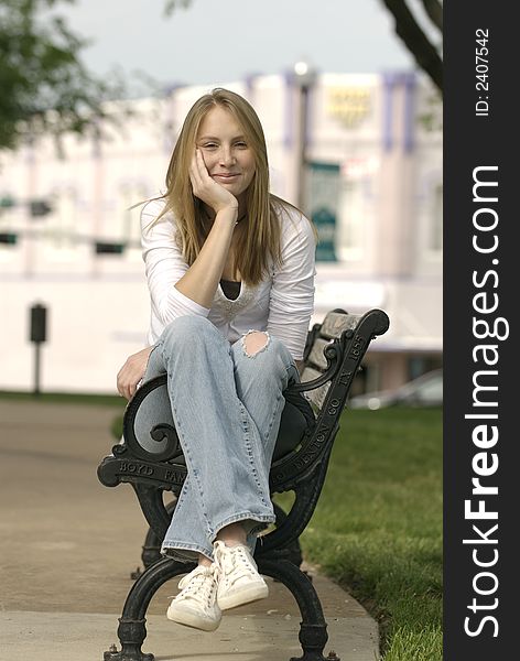 A caucasian female American teenager sits on a park bench on the Square in a small Texas town.