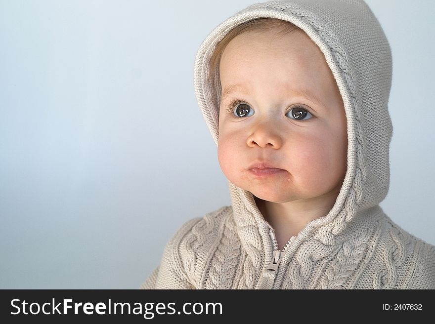 Image of cute baby wearing a hooded sweater, sitting in front of a white background. Image of cute baby wearing a hooded sweater, sitting in front of a white background