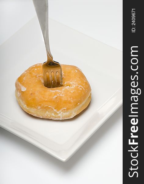 Single glazed donut on white plate with fork sticking out. Single glazed donut on white plate with fork sticking out