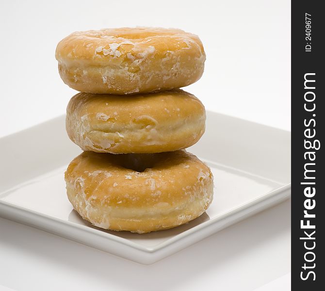 Three glazed donuts stacked on white plate